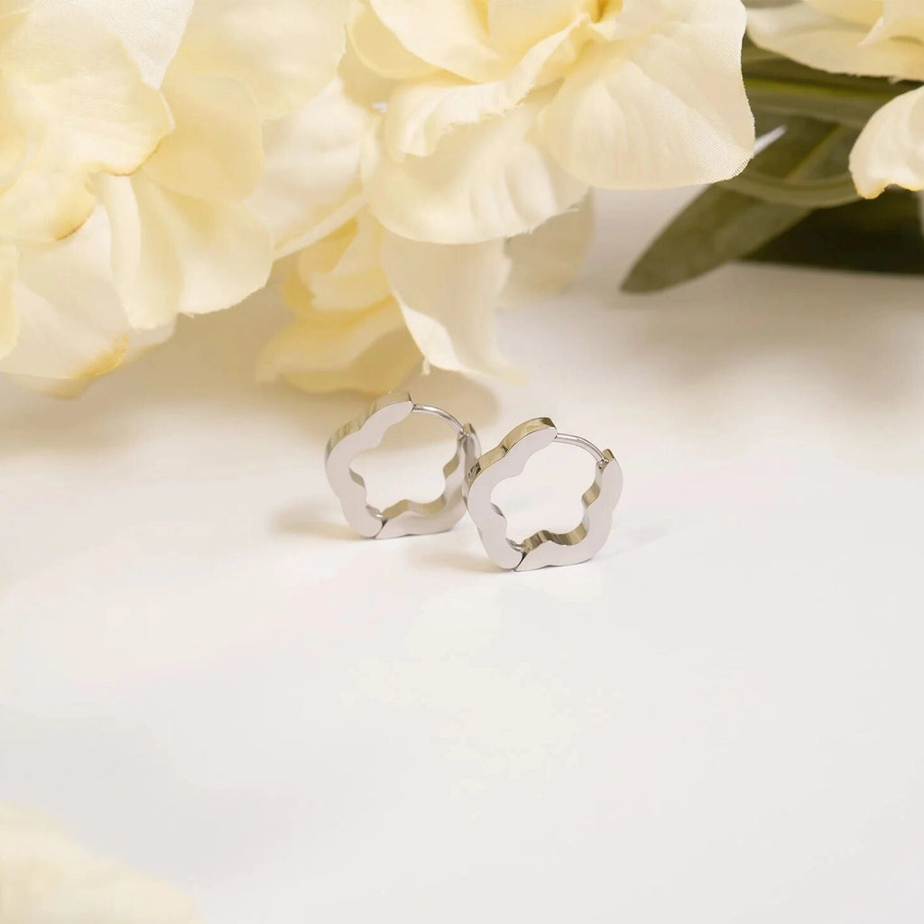 Paire de boucles d’oreilles Flora argentées devant des fleurs blanches