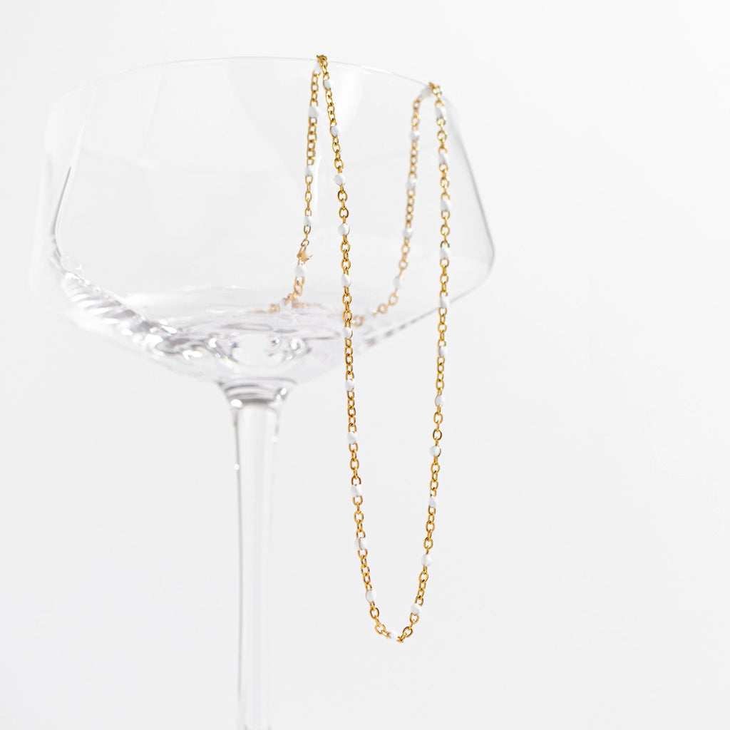 Collier Confetti Blanc doré présenté sur une coupe en verre